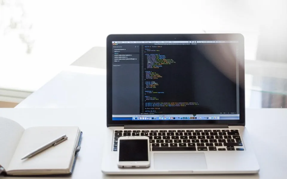 Computadora portátil, teléfono y libreta sobre un escritorio blanco